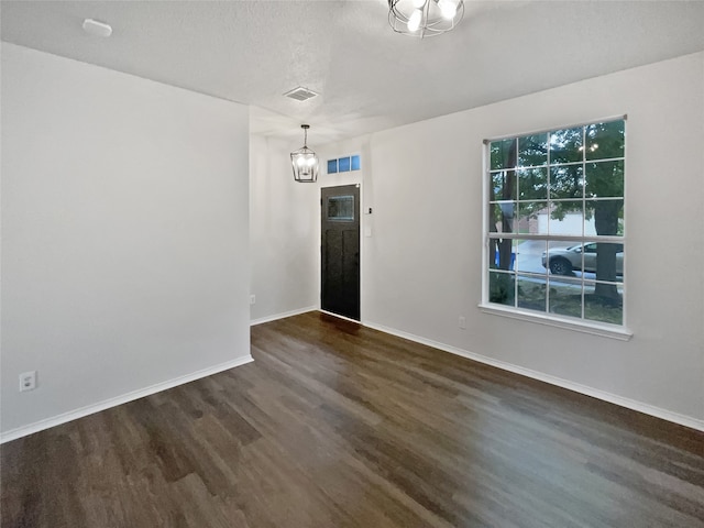 spare room featuring a textured ceiling, dark wood-type flooring, and a notable chandelier