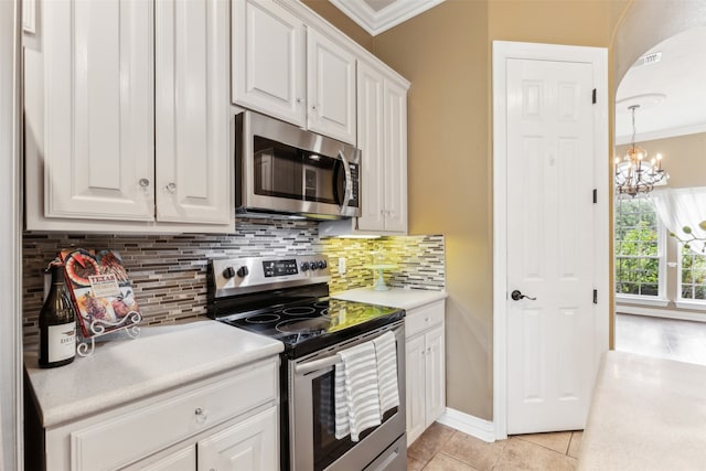 kitchen with appliances with stainless steel finishes, white cabinets, light tile patterned floors, ornamental molding, and a notable chandelier