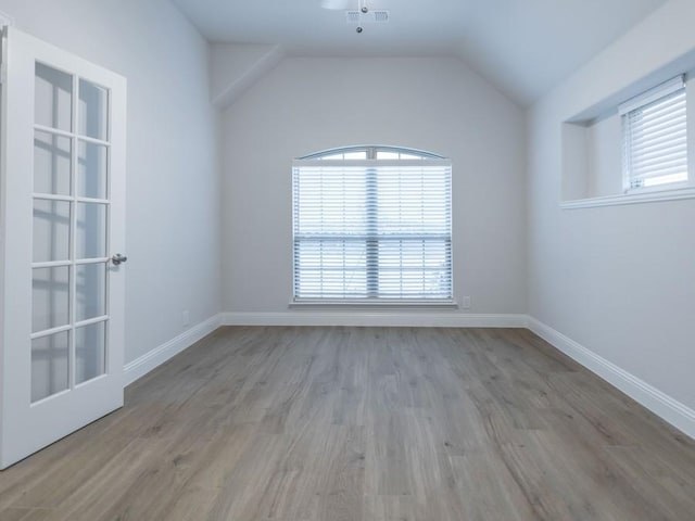 spare room featuring plenty of natural light, vaulted ceiling, and light hardwood / wood-style flooring