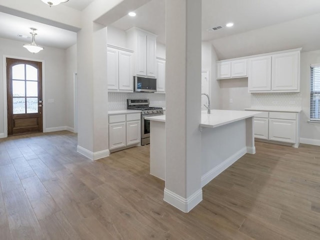 kitchen featuring light wood-type flooring, backsplash, stainless steel appliances, white cabinets, and hanging light fixtures