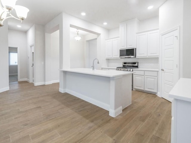 kitchen with decorative backsplash, light wood-type flooring, stainless steel appliances, decorative light fixtures, and white cabinets