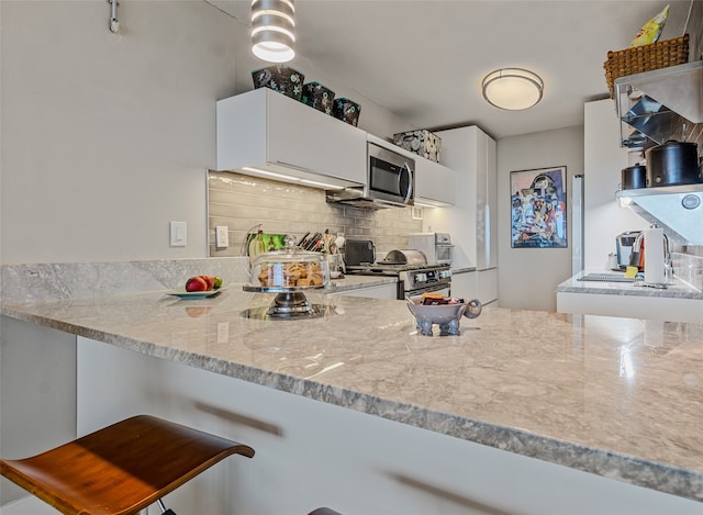 kitchen with white cabinetry, tasteful backsplash, a kitchen bar, kitchen peninsula, and appliances with stainless steel finishes