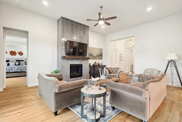 living room featuring light hardwood / wood-style floors, a tile fireplace, and ceiling fan