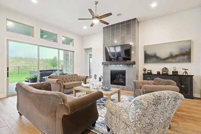 living room with light wood-type flooring, ceiling fan, and a tile fireplace