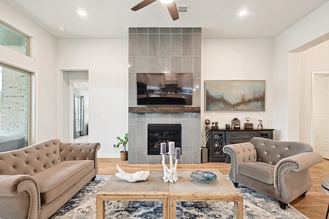 living room with a tile fireplace, light hardwood / wood-style floors, and ceiling fan