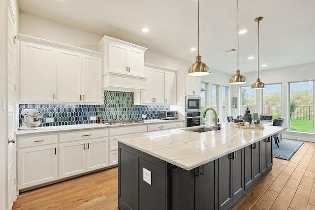 kitchen with white cabinetry, light hardwood / wood-style flooring, stainless steel appliances, a center island with sink, and decorative light fixtures