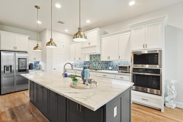 kitchen featuring an island with sink, stainless steel appliances, and white cabinets