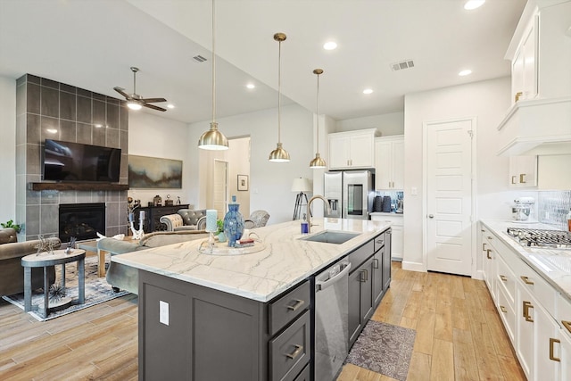 kitchen featuring a kitchen island with sink, white cabinetry, a tiled fireplace, and ceiling fan