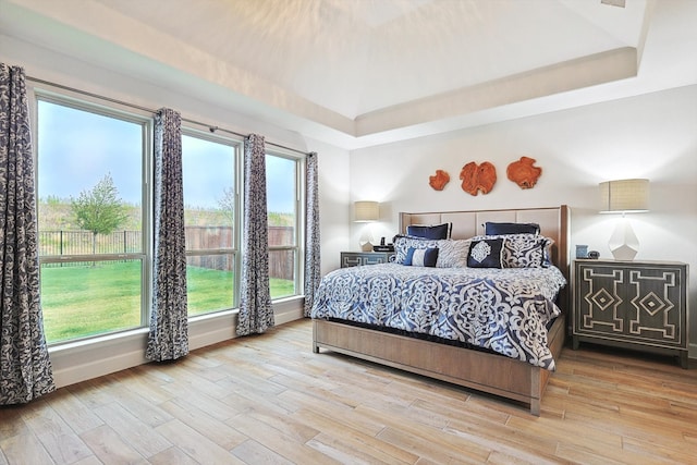 bedroom featuring wood-type flooring, a raised ceiling, and multiple windows