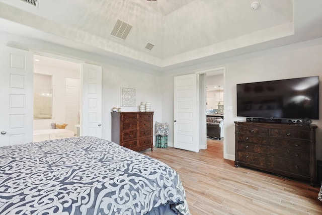 bedroom with light hardwood / wood-style flooring, a tray ceiling, and ensuite bathroom