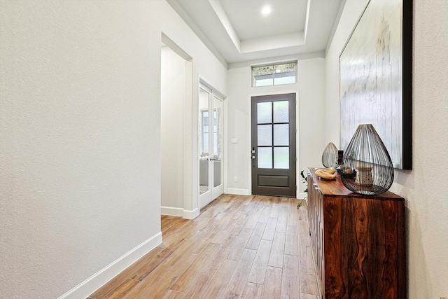 entryway with light wood-type flooring and a raised ceiling