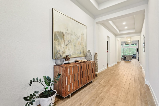 hall featuring light hardwood / wood-style flooring, a chandelier, and a tray ceiling