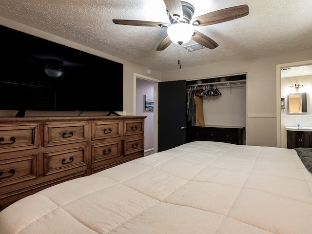 bedroom with a textured ceiling, a closet, ensuite bathroom, sink, and ceiling fan