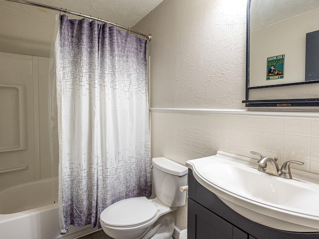 bathroom featuring a textured ceiling, a textured wall, toilet, vanity, and shower / bath combo with shower curtain