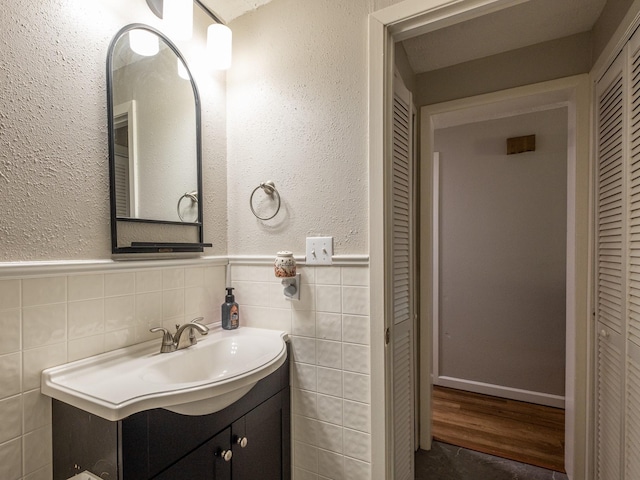 bathroom with a textured wall, a wainscoted wall, vanity, tile walls, and a closet