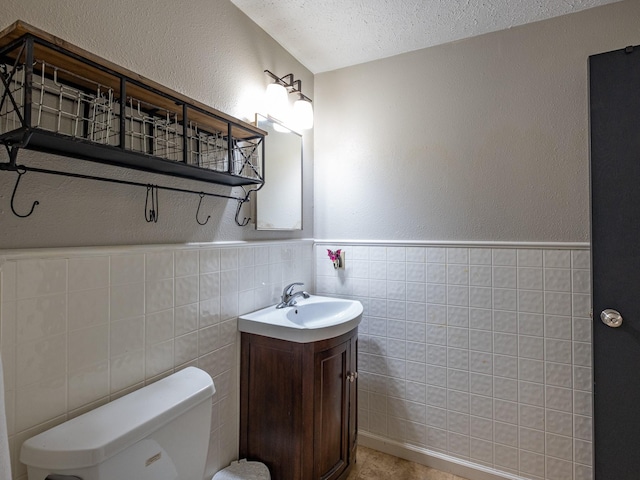 bathroom featuring toilet, a wainscoted wall, a textured ceiling, vanity, and tile walls