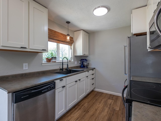 kitchen featuring dark wood finished floors, stainless steel appliances, dark countertops, white cabinetry, and a sink