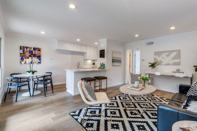 living room featuring ornamental molding, sink, and light hardwood / wood-style floors