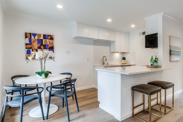 kitchen featuring white cabinets, kitchen peninsula, light hardwood / wood-style flooring, backsplash, and crown molding