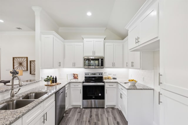 kitchen featuring appliances with stainless steel finishes, backsplash, vaulted ceiling, sink, and white cabinetry