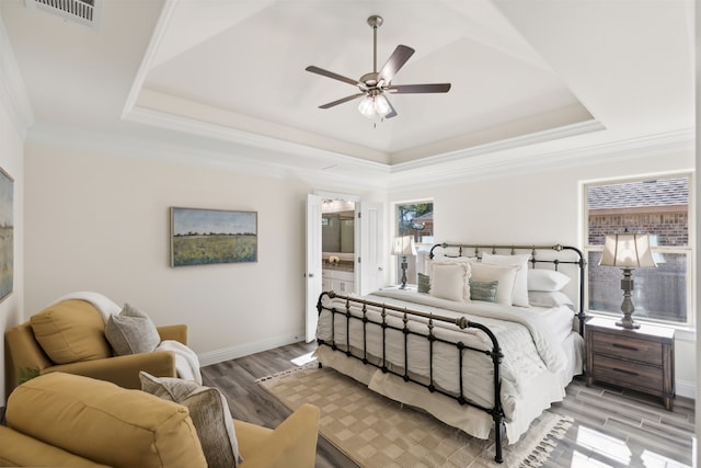 bedroom with crown molding, ceiling fan, light wood-type flooring, connected bathroom, and a tray ceiling