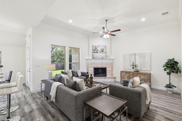 living room with ceiling fan, a fireplace, ornamental molding, and hardwood / wood-style flooring