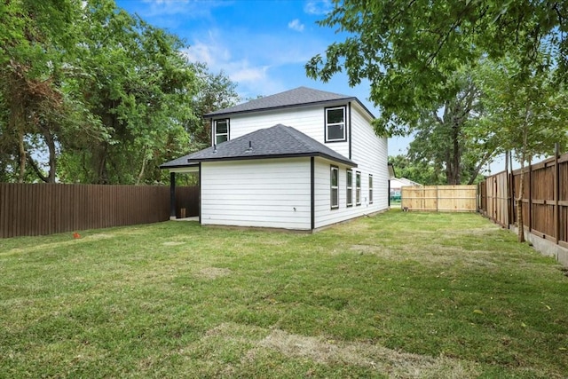 rear view of house with a shingled roof, a fenced backyard, and a lawn