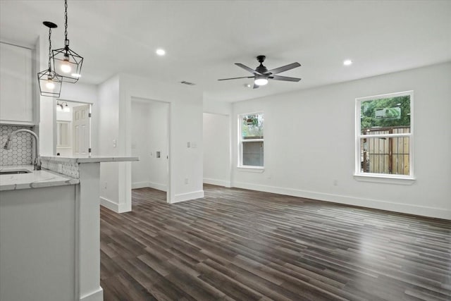 unfurnished living room with ceiling fan, dark wood-type flooring, a healthy amount of sunlight, and sink