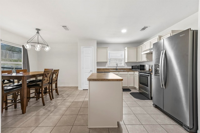 kitchen featuring light tile patterned floors, stainless steel appliances, a center island, decorative light fixtures, and sink