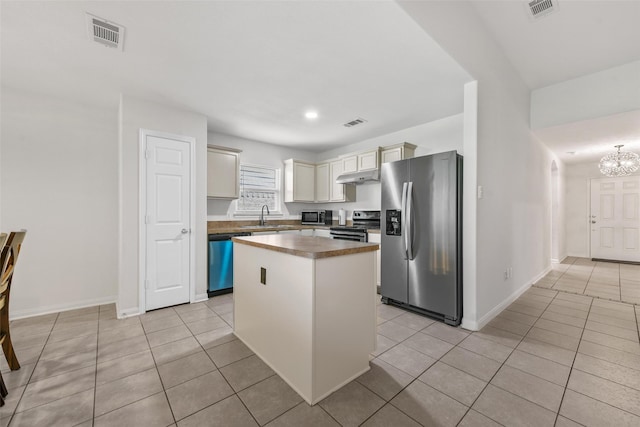 kitchen with a kitchen island, light tile patterned floors, stainless steel appliances, sink, and a notable chandelier