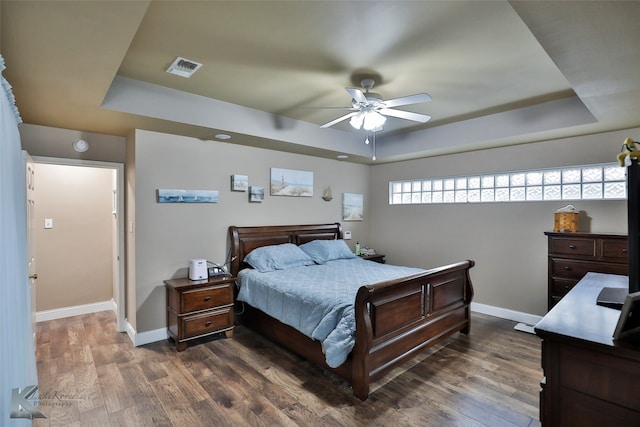 bedroom with dark hardwood / wood-style flooring, ceiling fan, and a raised ceiling