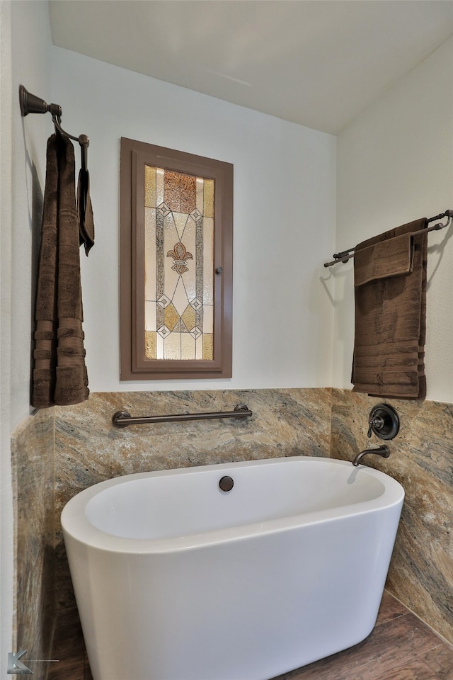 bathroom featuring tile walls, hardwood / wood-style floors, and a bathtub