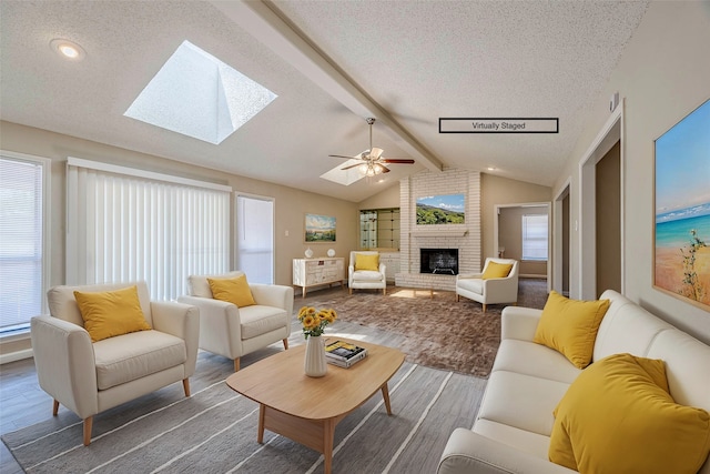 living room featuring a brick fireplace, a textured ceiling, lofted ceiling with skylight, ceiling fan, and dark hardwood / wood-style floors