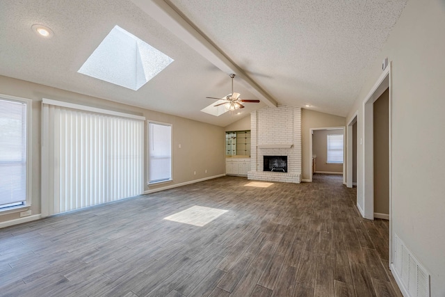 unfurnished living room featuring a fireplace, hardwood / wood-style floors, lofted ceiling with skylight, and ceiling fan