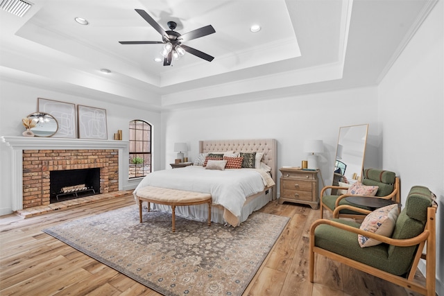 bedroom featuring ceiling fan, a fireplace, light hardwood / wood-style floors, and a raised ceiling