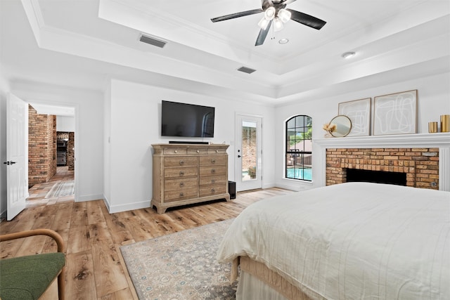 bedroom with light wood-type flooring, crown molding, a brick fireplace, ceiling fan, and a tray ceiling