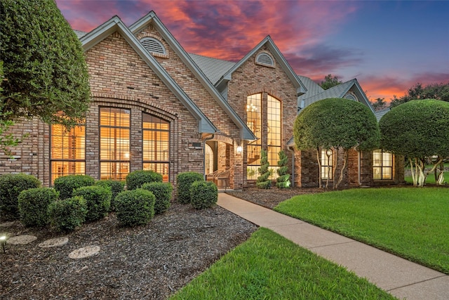 view of front of home featuring brick siding and a yard