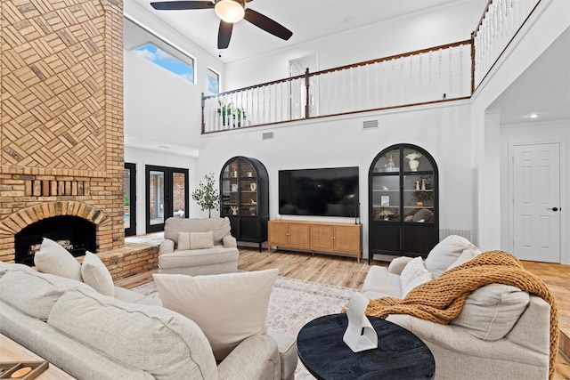 living room featuring crown molding, a brick fireplace, light hardwood / wood-style floors, ceiling fan, and a towering ceiling