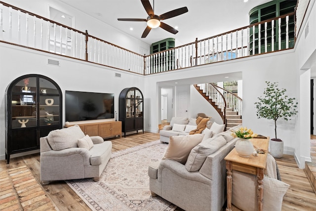 living room with ceiling fan, a towering ceiling, and light wood-type flooring