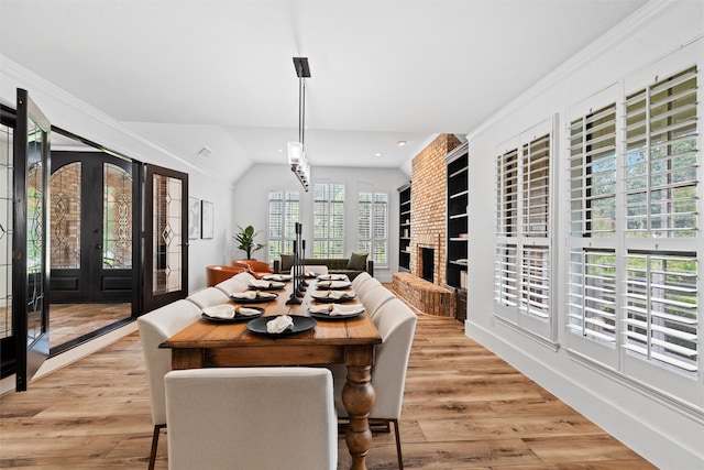 dining area featuring ornamental molding, a brick fireplace, french doors, lofted ceiling, and light hardwood / wood-style floors