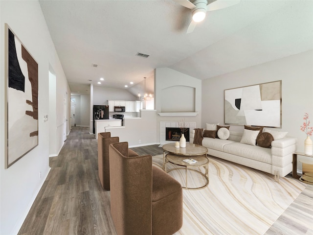 living room featuring lofted ceiling, ceiling fan, a tile fireplace, and dark hardwood / wood-style floors