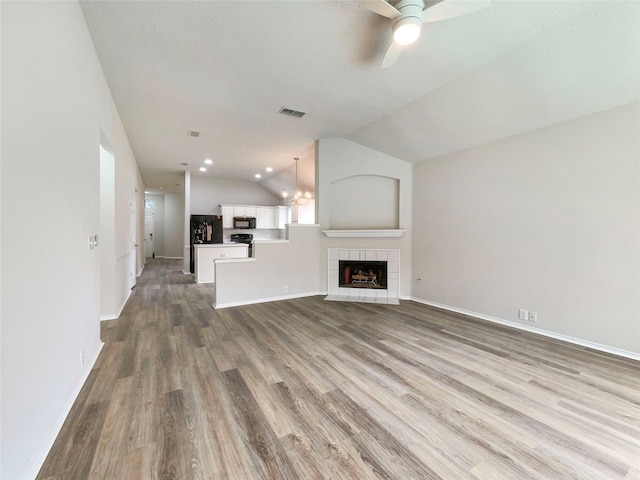 unfurnished living room featuring a textured ceiling, vaulted ceiling, a tiled fireplace, light hardwood / wood-style flooring, and ceiling fan