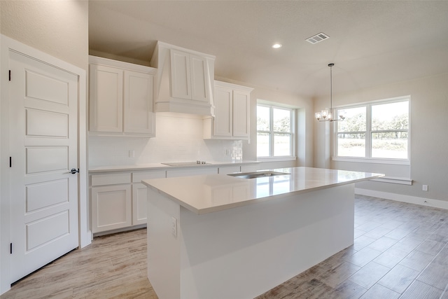 kitchen featuring an inviting chandelier, backsplash, decorative light fixtures, an island with sink, and white cabinets