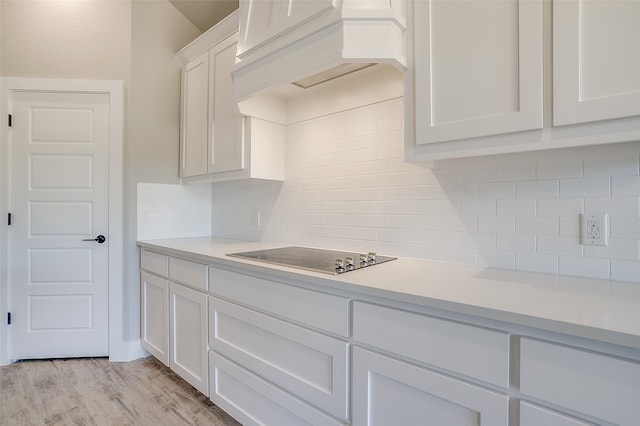 kitchen featuring premium range hood, white cabinetry, decorative backsplash, light hardwood / wood-style floors, and black electric cooktop