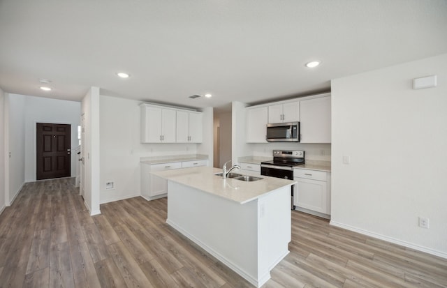 kitchen with stainless steel appliances, sink, light hardwood / wood-style floors, white cabinetry, and an island with sink