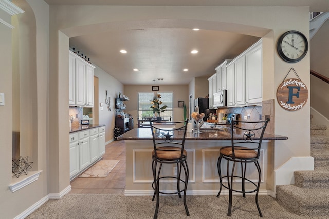 kitchen with kitchen peninsula, backsplash, stainless steel appliances, white cabinets, and a breakfast bar area