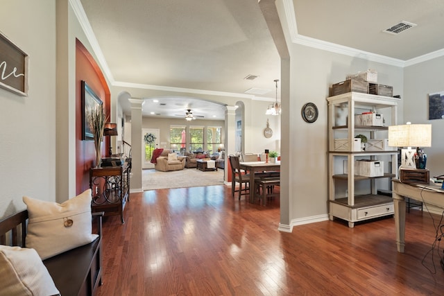 living room with wood-type flooring, ceiling fan with notable chandelier, ornate columns, and crown molding