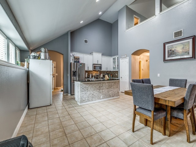 kitchen with light tile patterned floors, tasteful backsplash, stainless steel appliances, high vaulted ceiling, and white cabinets