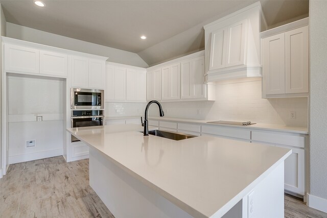 kitchen featuring a kitchen island with sink, white cabinetry, sink, and vaulted ceiling