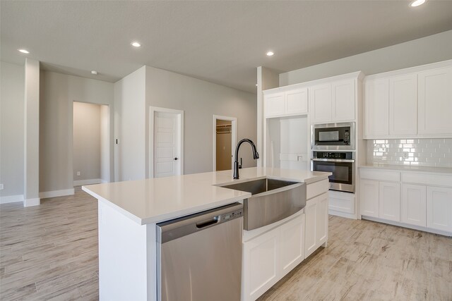 kitchen with white cabinets, appliances with stainless steel finishes, backsplash, and an island with sink